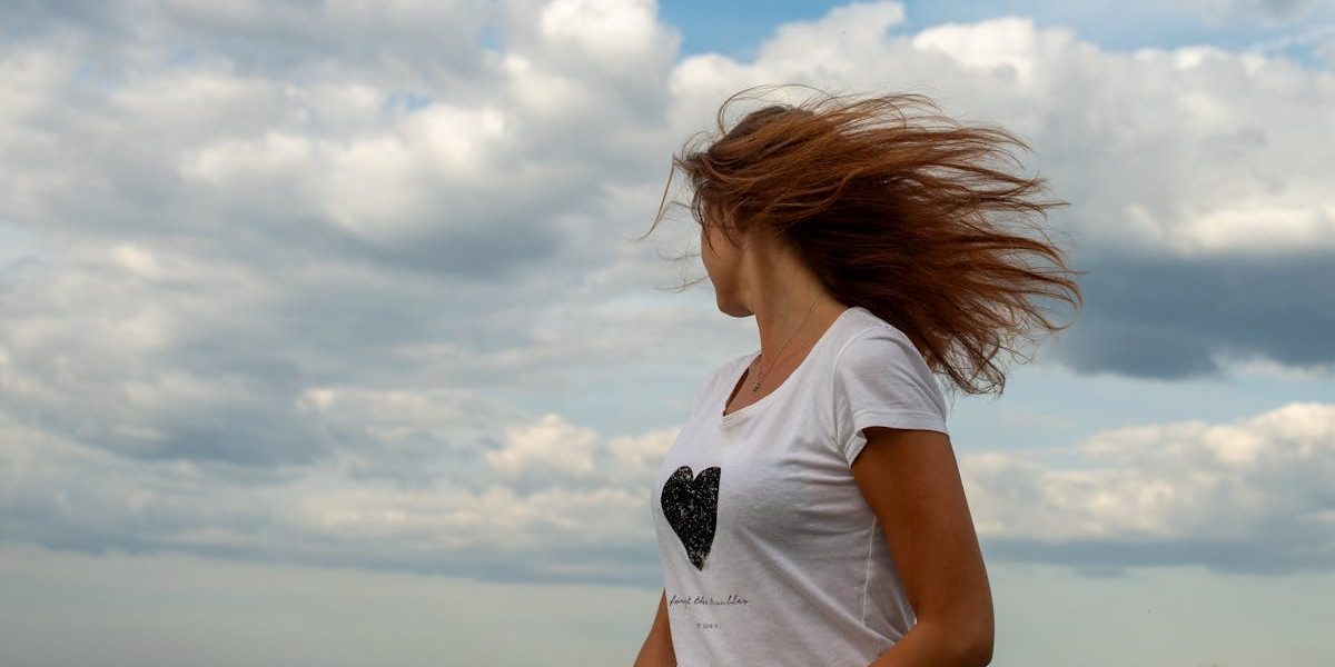 Woman with blowing hair stands by Tallinn seaside under dramatic cloudy sky.