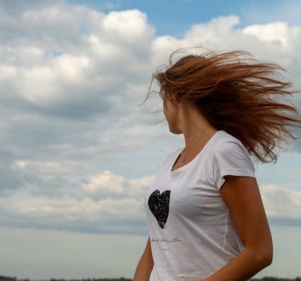 Woman with blowing hair stands by Tallinn seaside under dramatic cloudy sky.