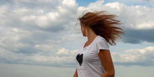 Woman with blowing hair stands by Tallinn seaside under dramatic cloudy sky.