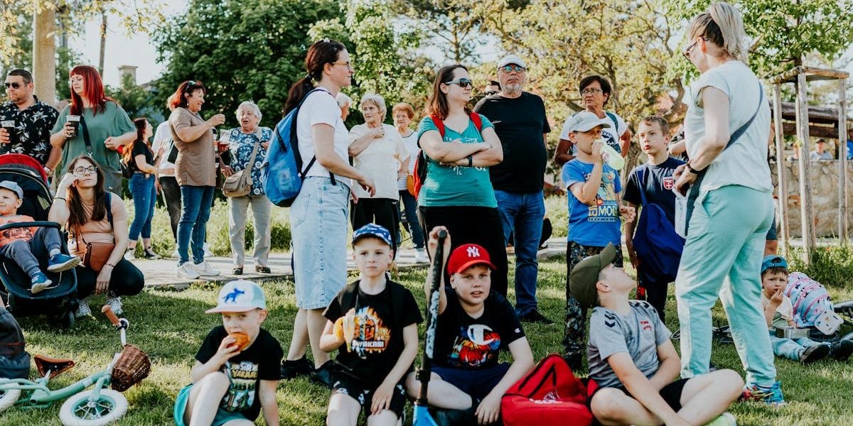 A diverse group of families and children enjoying an outdoor event on a sunny day in a park setting.