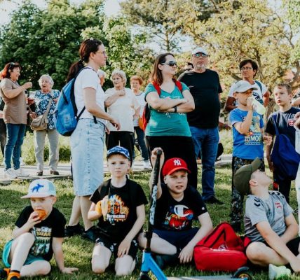 A diverse group of families and children enjoying an outdoor event on a sunny day in a park setting.