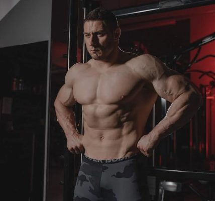 Shirtless bodybuilder flexing muscles under dramatic gym lighting. Fitness and strength.